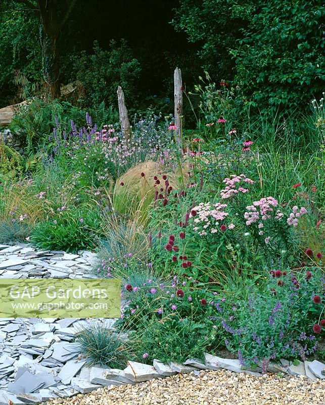 Walled garden in Devon with wooden bench, Stipa tenuissima, slate, Monarda 'Beauty of Cobham', Scabiosa columbaria 'Nana' and Achillea 'Love Parade'