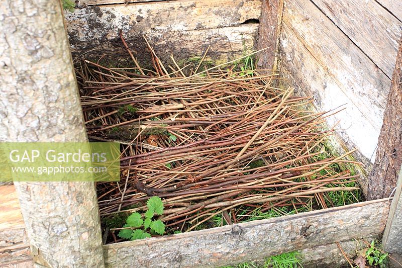 A compost bin filled with a layer of thin branches which allows air into the bottom of the heap