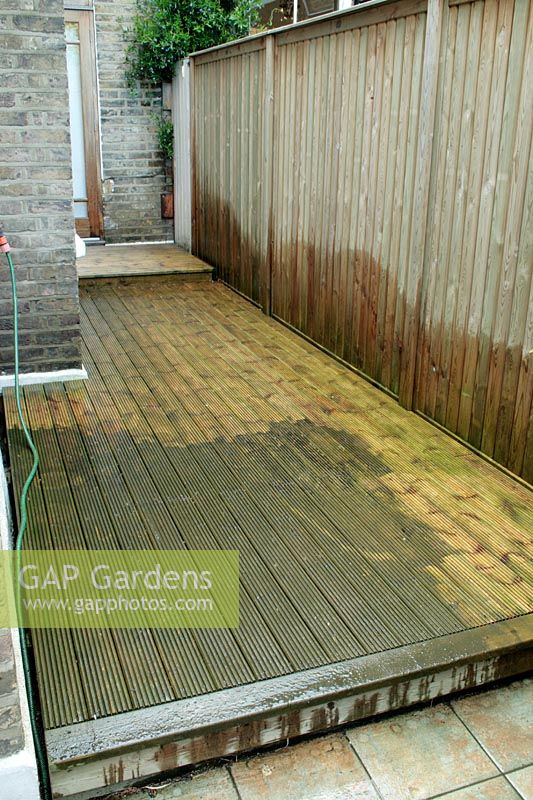 Area of decking down the side of a terraced town house in the process of being cleaned using a pressure washer.