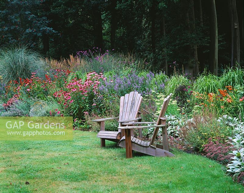 Seping border beside wooden adirondack chairs with Echinacea, Nepeta and ornamental grasses - Greystone Cottage, Oxfordshire