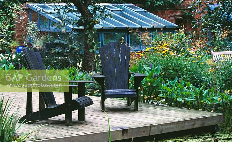 Decking beside pond with adirondack chairs and greenhouse in the background - Greystone Cottage, Oxfordshire