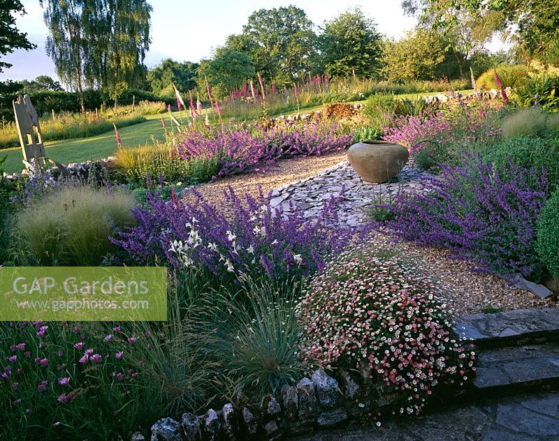 The gravel garden with Erigeron, Nepeta 'Walkers Low', Stipa tenuissima, slate bed with large empty container and wooden throne chair - Clare Matthews garden, Devon
