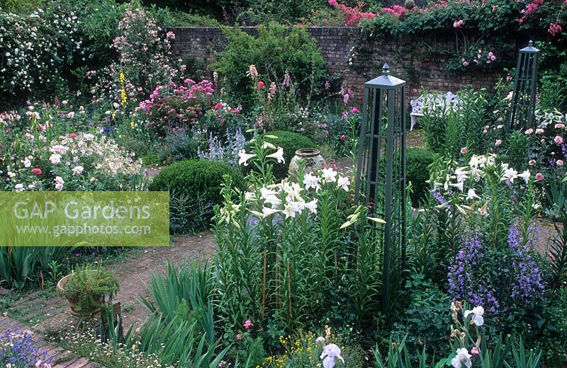 Walled flower garden with obelisk, Rosa, Campanula Lilium, Nicotiana and white metal garden bench - Rustenberg Garden, South Africa