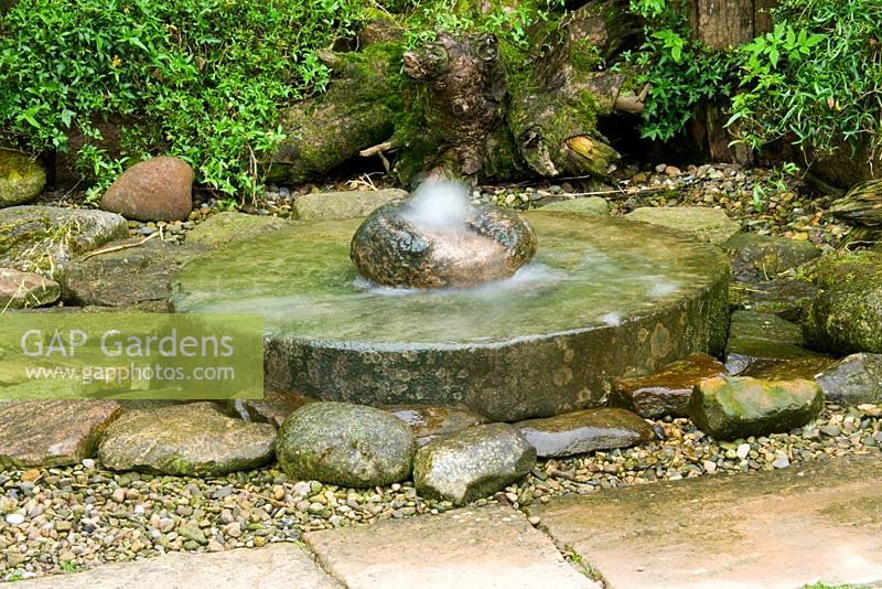 Millstone water feature surrounded by ferns, gravel and rocks - Hunmanby Grange, Yorkshire