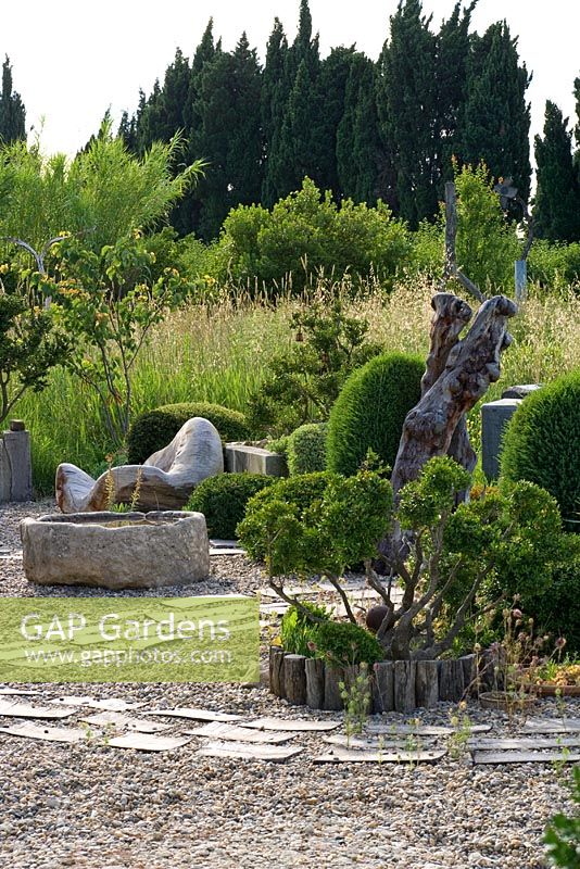 Gravel garden with clipped box, stone water container and beautiful wooden sculpted seat - Provence, France