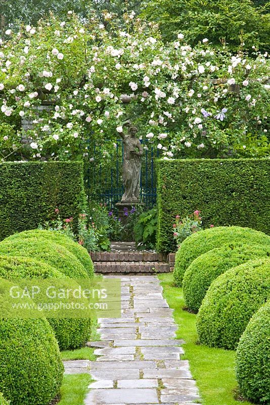 Formal garden with wooden pergola and climbing Rosa 'New Dawn', clipped Taxus and Buxus hedging with view to stone statue