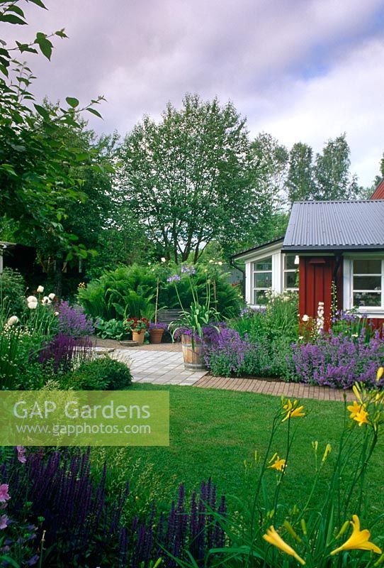 Colour themed border with Salvia, Nepeta and Hemerocallis, lawn and patio area with pots and containers - Ulf Nordfjell's garden, Agnas, Sweden
