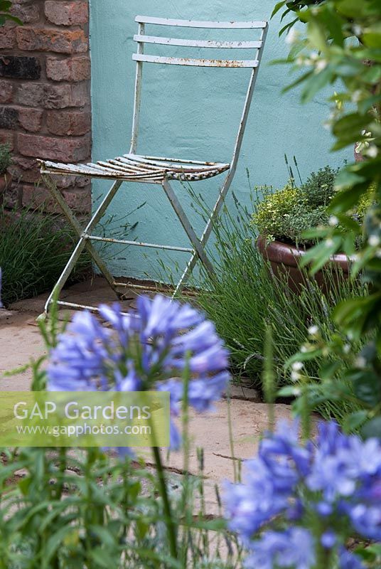 Chair on stone patio with herbs in the The Scented Walled Garden and Agapanthus in foreground, Exhibitor - Arley Hall at RHS Tatton Flower Show 2008