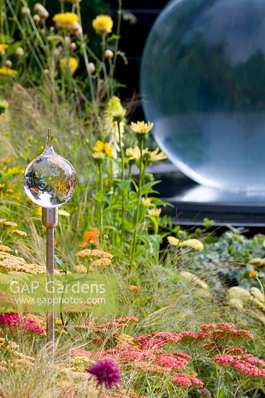 Achillea and Leucanthemum in warm colour border reflecting glass globes on aluminium spikes. Large glass globe water feature - Benecol's Prism Corner Garden - supporting Rainbow Trust - RHS Hampton Court Flower Show 2008