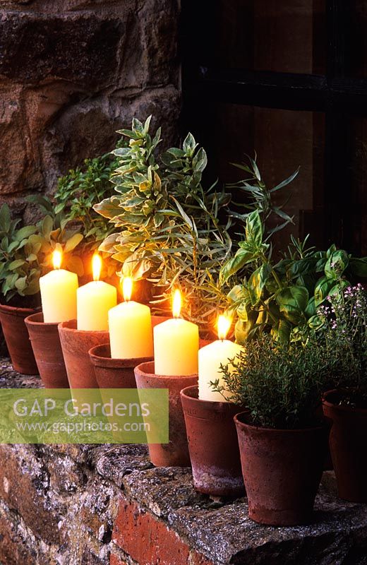 Candles in terracotta pots on windowsill with potted herbs - The Oast Houses, Hampshire