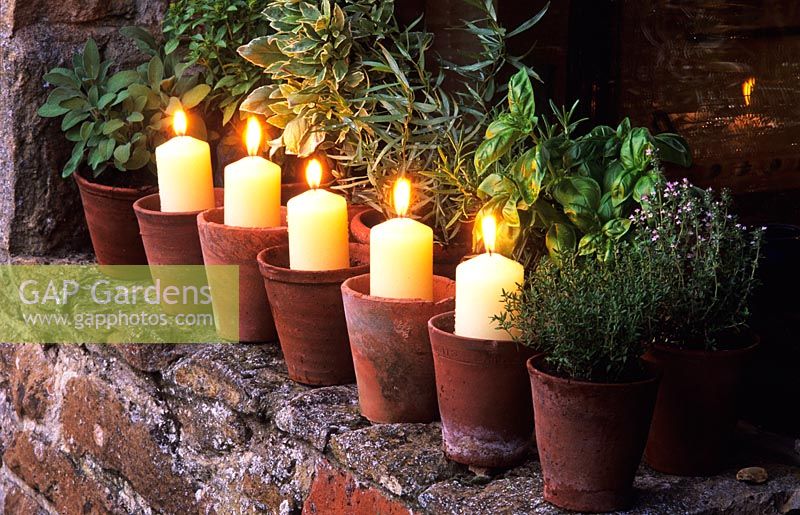 Candles in terracotta pots on windowsill with potted herbs - The Oast Houses, Hampshire.