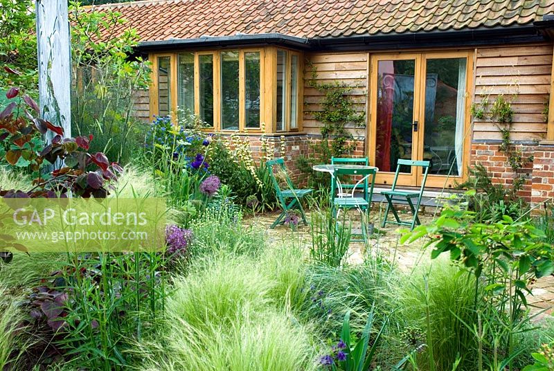 Terrace with seating area, mixed border includes Stipa tenuissima, Allium, Iris and Cercis canandensis 'Forest Pansy'