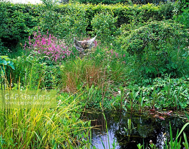 Mixed aquatic planting near pond, figurative sculpture amongst flowerbed - Kingswood Cottages, Buckinghamshire