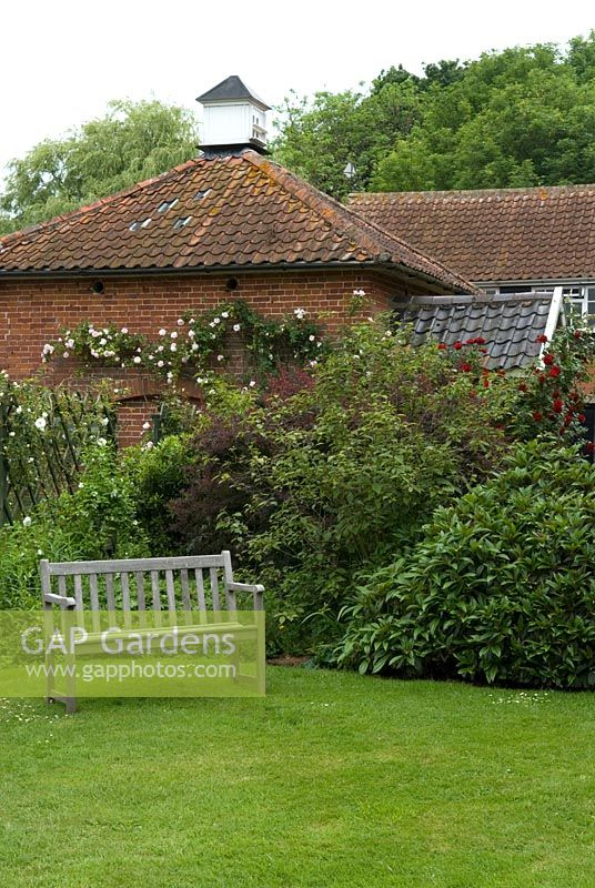Wooden seat with border shrubs in front of old brick dovecote on Suffolk farm - Earl Soham Open Gardens 2007