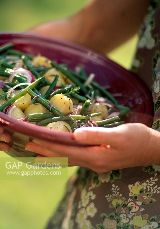 Woman carrying bowl of potato salad with green beans and red onions