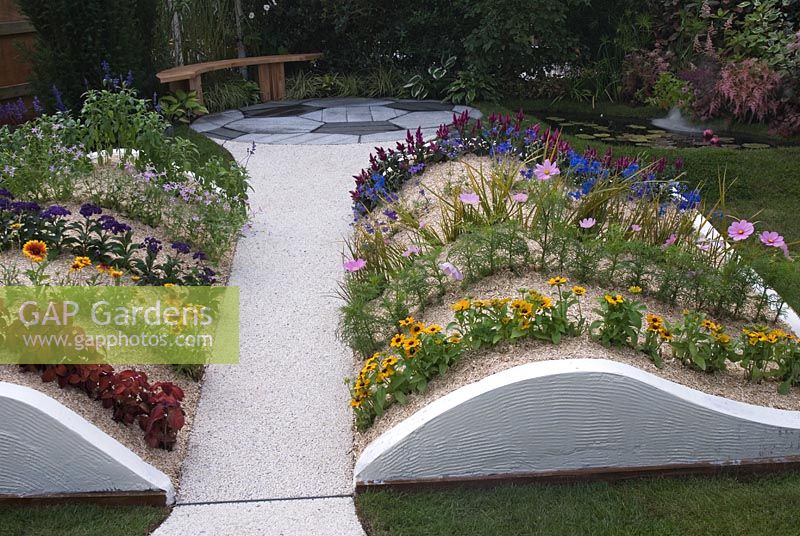 Seating area, small pond and rows of flowers in curved beds with bark chippings in the 'Liverpool Success Story' garden by Abel Landscapes at Southport Flower Show 2008