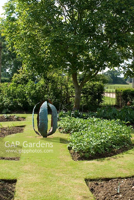 Copper seed pod in vegetable garden by Carrie Norman, plantings of potatoes in horseshoe beds - Lucy Redman's School of Garden Design