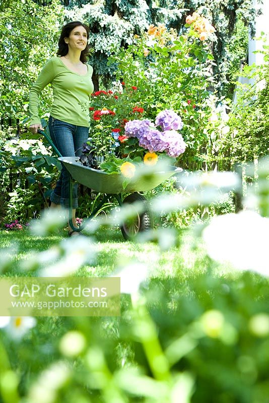 Woman in garden pushing wheelbarrow full of pots of flowers