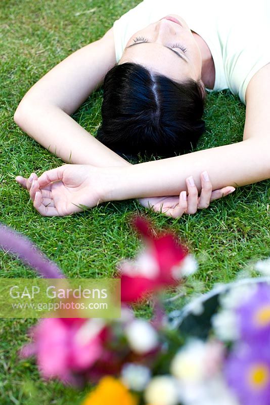 Woman lying on lawn beside bucket of flowers