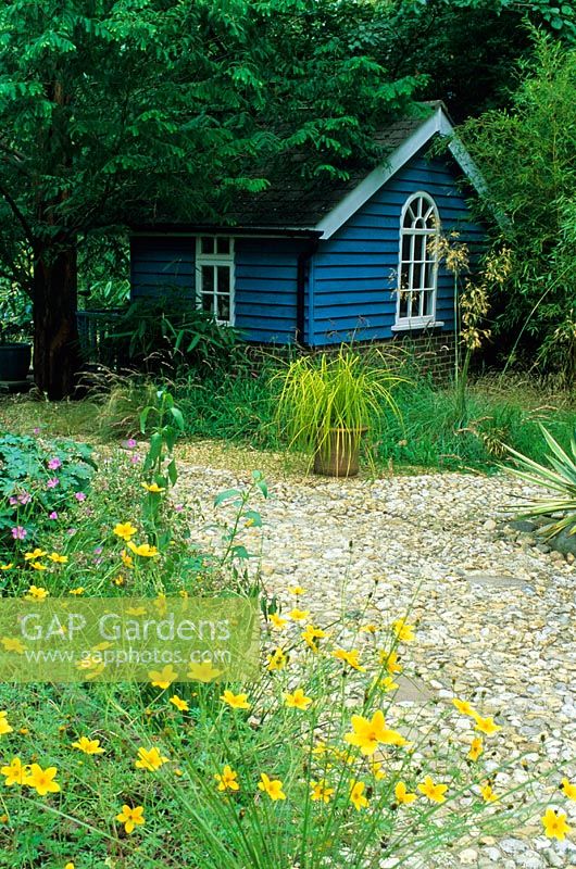 Blue painted summer house under trees with gravel garden. Designed by Alan Titchmarsh at Barleywood, Hampshire.