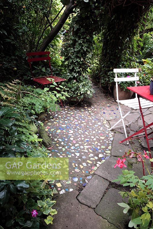 Mosaic paving from plate shards on shady patio, folding chairs and shade loving plants - Begonia, Hedera and Ferns