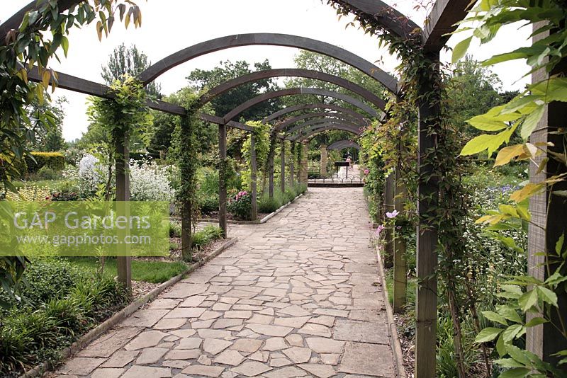 Wooden arch Pergola with Wisteria and Clematis, crazy paving of Yorkstone - Sexby Garden, Peckham Rye Park, London, heritage lottery fund