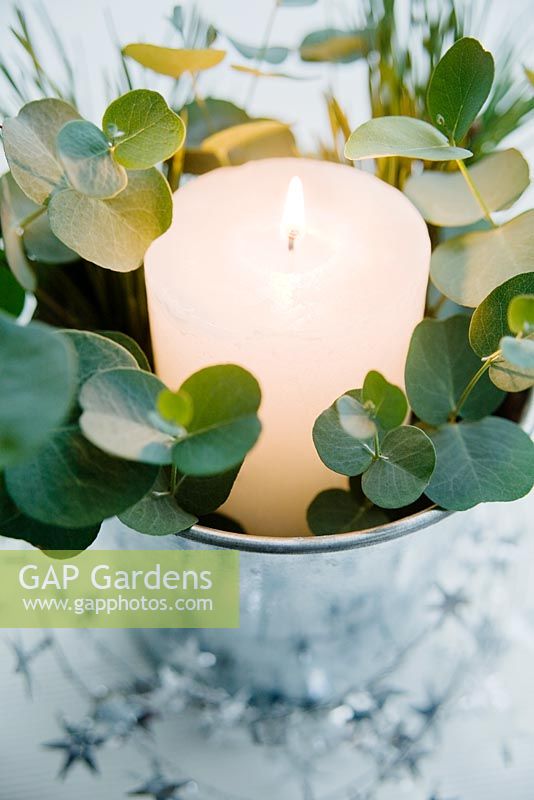 Table decoration of white candle in silver zinc bucket with eucalyptus foliage