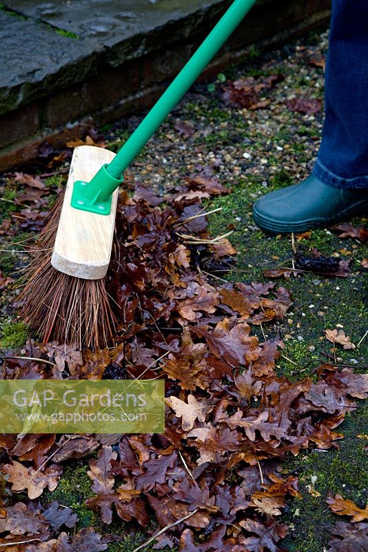 Woman sweeping leaves with coarse broom