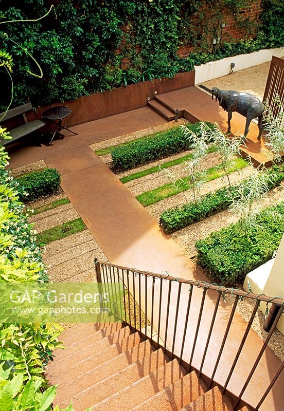 Corten steel predominates in this London garden, used for the paths and stairs here. Strip plantings of lawn, box and gravel along with walls greened with climbers create a foil. Willows grow through the Buxus.