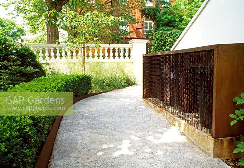 Corten steel is used throughout this London garden. Here it boarders the paths, and creates a storage area for the rubbish bins, further disgused by a chain-link curtain.