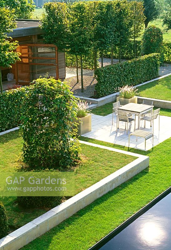 This aerial view reveals the layers and divisions of this otherwise flat Belgium garden. Pleached hornbeams and hedging screens the garden room from the dinning terrace. Limestone blocks raise and boarder the lawn.