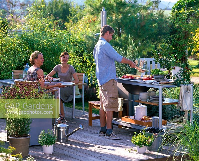 People in outdoor kitchen with pots with Origanum, Rosmarinus, Mentha and Laurus.