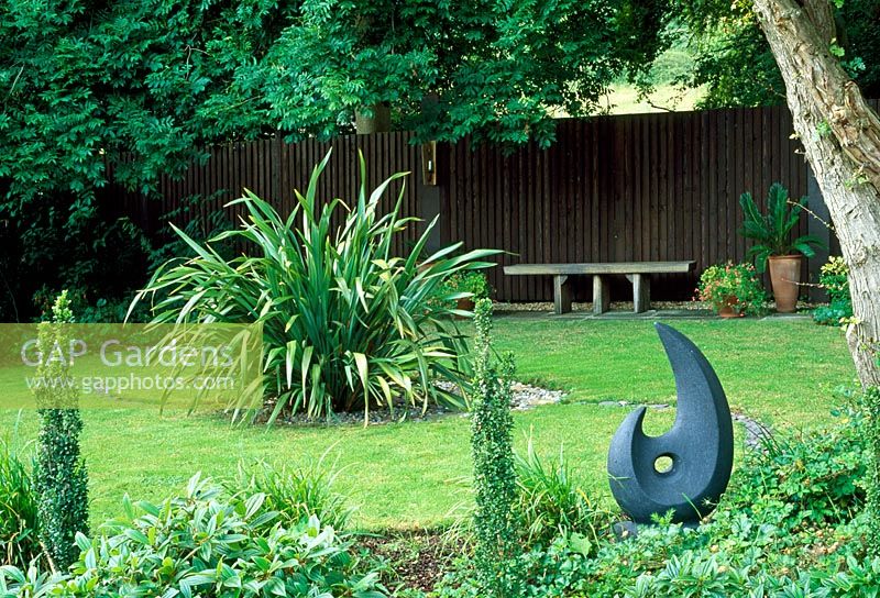 Phormium in sacred garden with black New Zealand sculpture and garden bench made of ash - Saltford Farm, Bath, UK