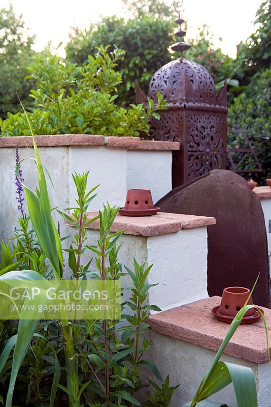 A Moroccan inspired garden with drought tolerant planting - Rendered wall with clay tiles, Moroccan lantern and small clay tea light holders