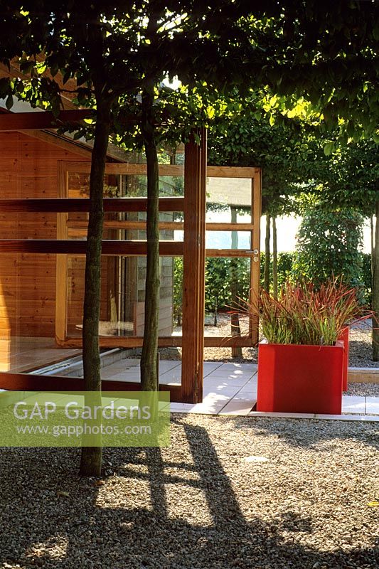 The garden room opens onto the dining terrace, screened by pleached hornbeam and hedging, red  fibreglass cube planters with Imperata cylindrica - Belgium