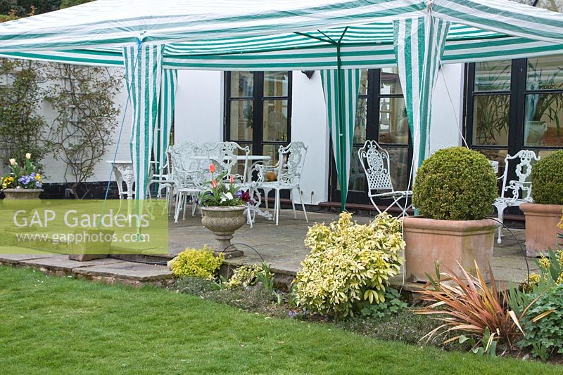 Patio area with white cast iron furniture under gazebo looking out onto lawns and garden - Millenium Garden, Lichfield, Staffordshire NGS