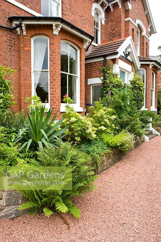 Front garden of a large detached house with red gravel driveway 