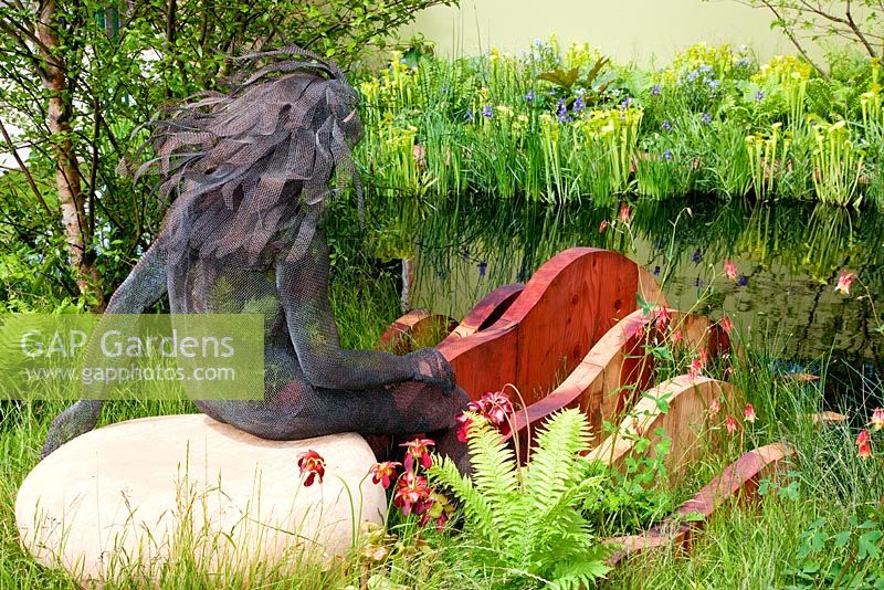 The Foreign and Colonial Investments Garden, Sponsored by Foreign and Colonial Investment Trust, Contractor The Outdoor Room - Silver Flora medal winner at RHS Chelsea Flower Show 2009.  Wire sculpture of girl on white boulder with redwood wave-form sculpture in front. Pool planting includes - pitcher plants Sarracenia flava, Iris x robusta 'Gerald Darby', Matteuccia struthiopteris, Aquilegia canadensis. 
