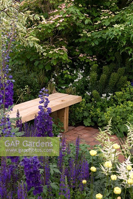 Wooden seat with lush planting of shrubs and herbaceous plants, 'A Plantsman's Palette' created by Roger Platts Garden Design and Nurseries. Winner of Silver-Gilt Floral Award in The Great Pavilion, Chelsea Flower Show 2009