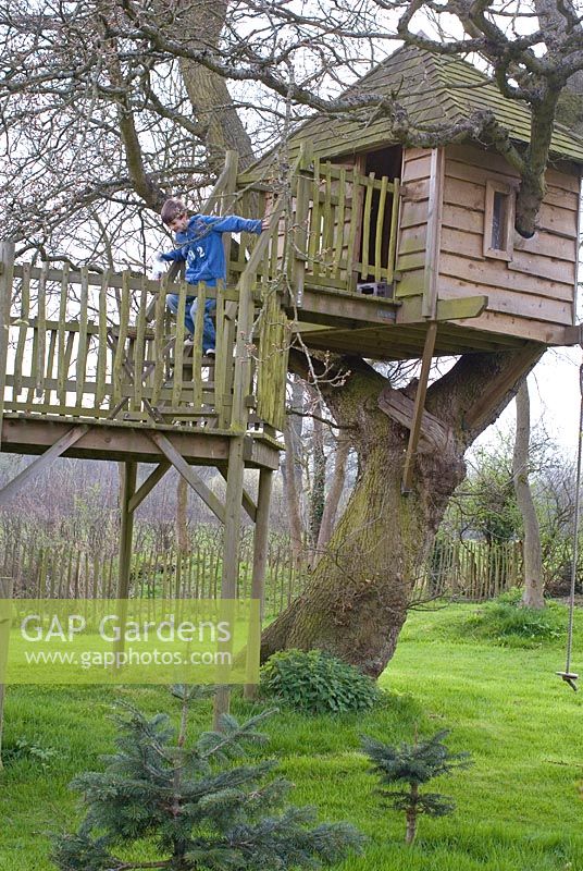 Wooden tree house with a rope swing and child running down the steps
