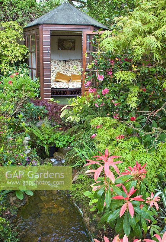 Summerhouse with mature Acers and shrubs with stream at Four Seasons NGS garden, Staffordshire