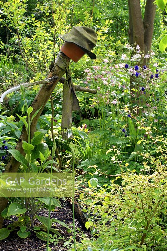 Rustic figurative sculpture made from driftwood amongst flowerbeds of Aquilegia and Digitalis - Columbines and foxgloves