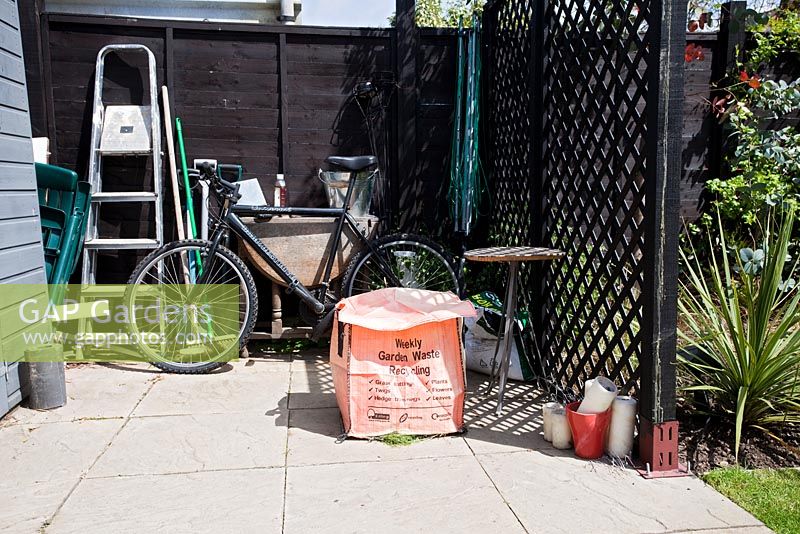 Utility area behind screen in garden with bike and garden waste bag - Small urban garden in London