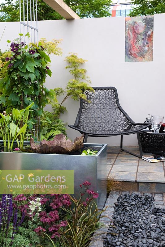 Black mesh chairs on a tiled patio with black pebbles, metal water feature and plants including, Astrantia major 'Claret', Salvia nemerosa 'Caradonna' and Eryngium bourgatii - An Urban Retreat by Paul Titcombe - BBC Gardeners' World Live 2009 - Gold Medallist 