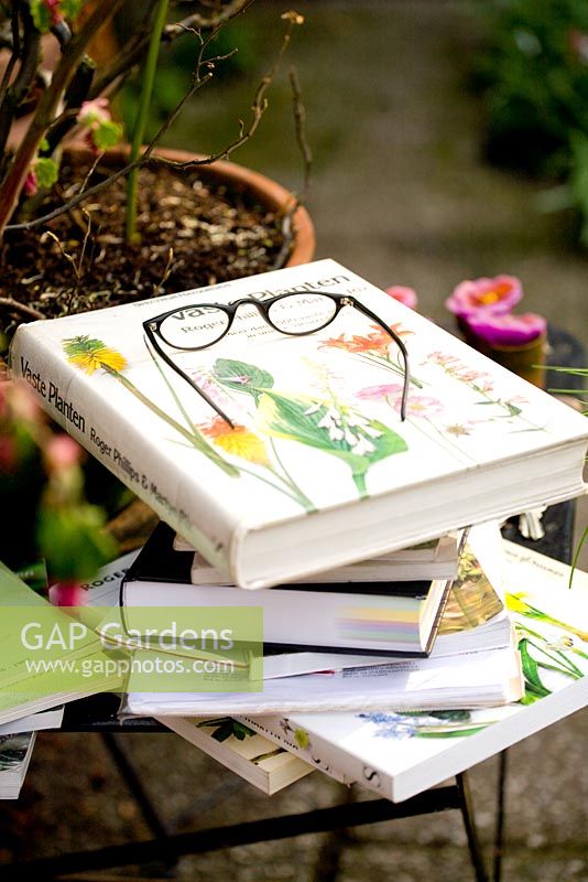Pair of reading glasses on pile of gardening books on table in garden