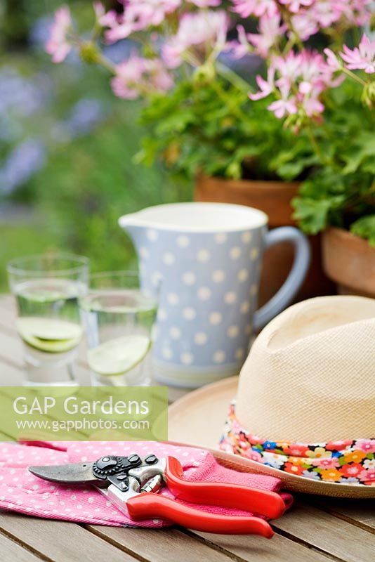 Sunhat and summer drinks on garden table with gardening gloves and secateurs