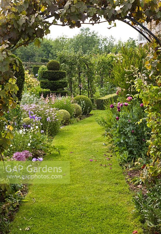 Grass pathway with borders of herbaceous perennials and rose arches with scented roses leading to the Potager and Knot Garden - Woodpeckers, Warwickshire