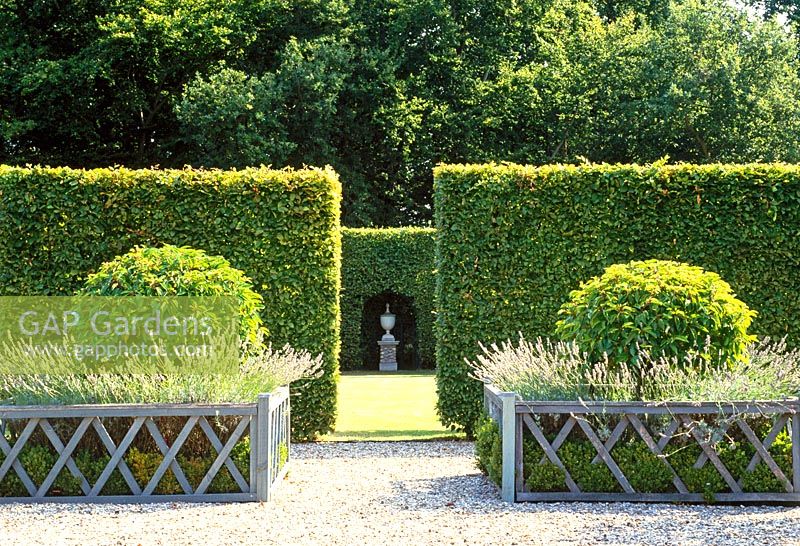 Geometry formalises a space. Tall beech linear hedges enclose a large space while outside decorative low wooden railings enclose box, lavender and green spheres 