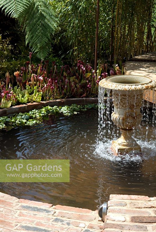 Cast iron garden urn used as water feature in circular pool with edging of carnivorous pitcher plants, bamboo and ferns. 'Modern Victorian Outdoor Space' Silver Flora award winning garden - Malvern Spring Show 2009
