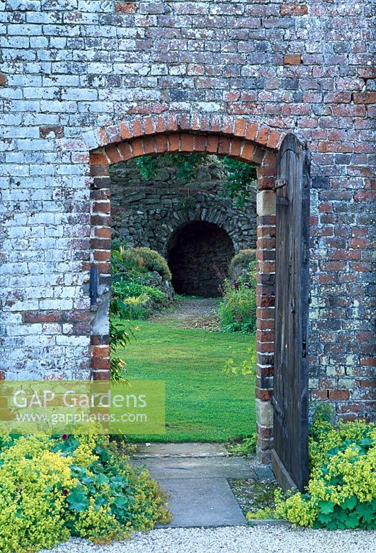 View through gateway to the walled Garden and the Grotto. Alchemilla mollis edges the gateway - Glansevern Hall Gardens, Welshpool, Wales in July